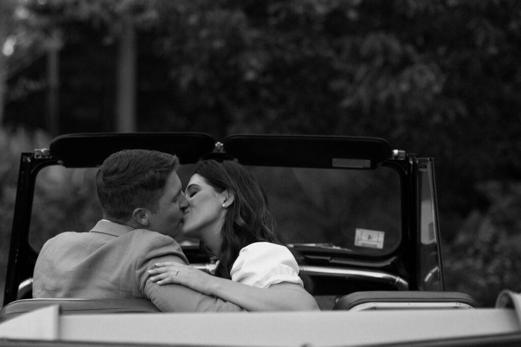 couple kiss in vintage car in black and white photo from Bradley Estate Engagement Photos