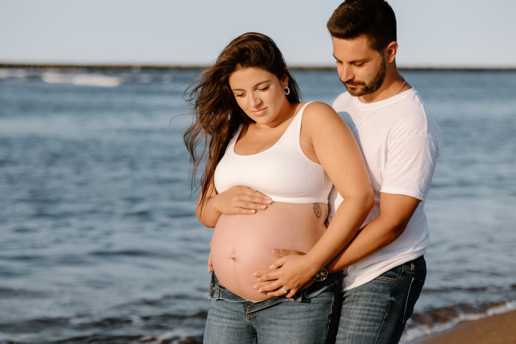husband and wife pose on the beach for maternity photos after preparing for a photoshoot