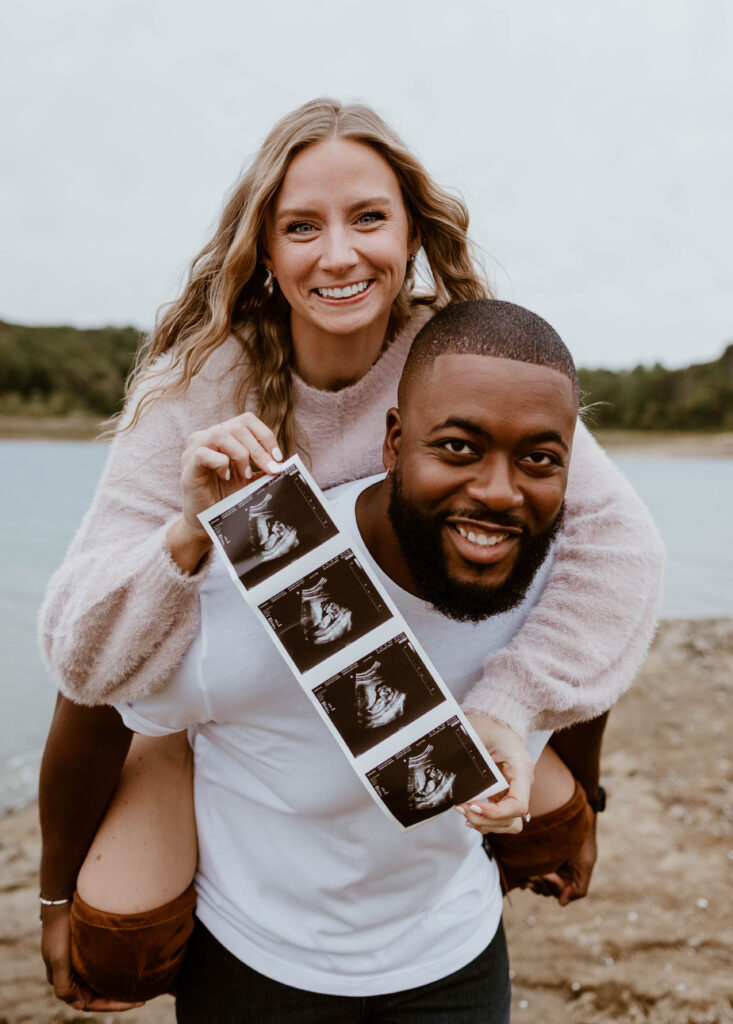 Husband gives wife a piggy back ride to announce they're having a baby during their fun pregnancy announcement photoshoot